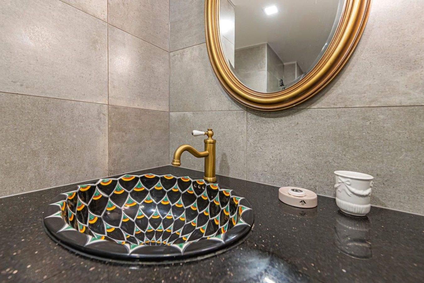 Un baño con un lavabo negro, grifo dorado y un espejo con marco dorado.