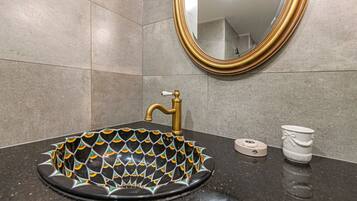 Un baño con un lavabo negro, grifo dorado y un espejo con marco dorado.