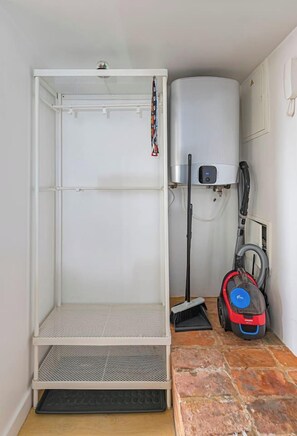 Une pièce équipée d'une étagère métallique, d'un aspirateur et d'un chauffe-eau.