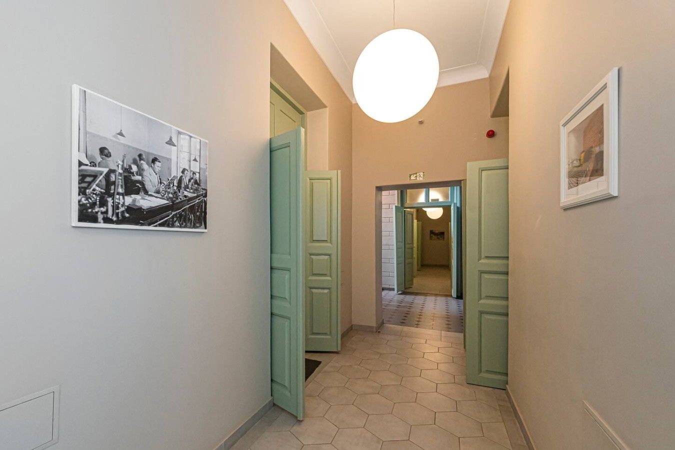 A hallway with hexagonal patterned flooring, green doors, and a round light fixture.