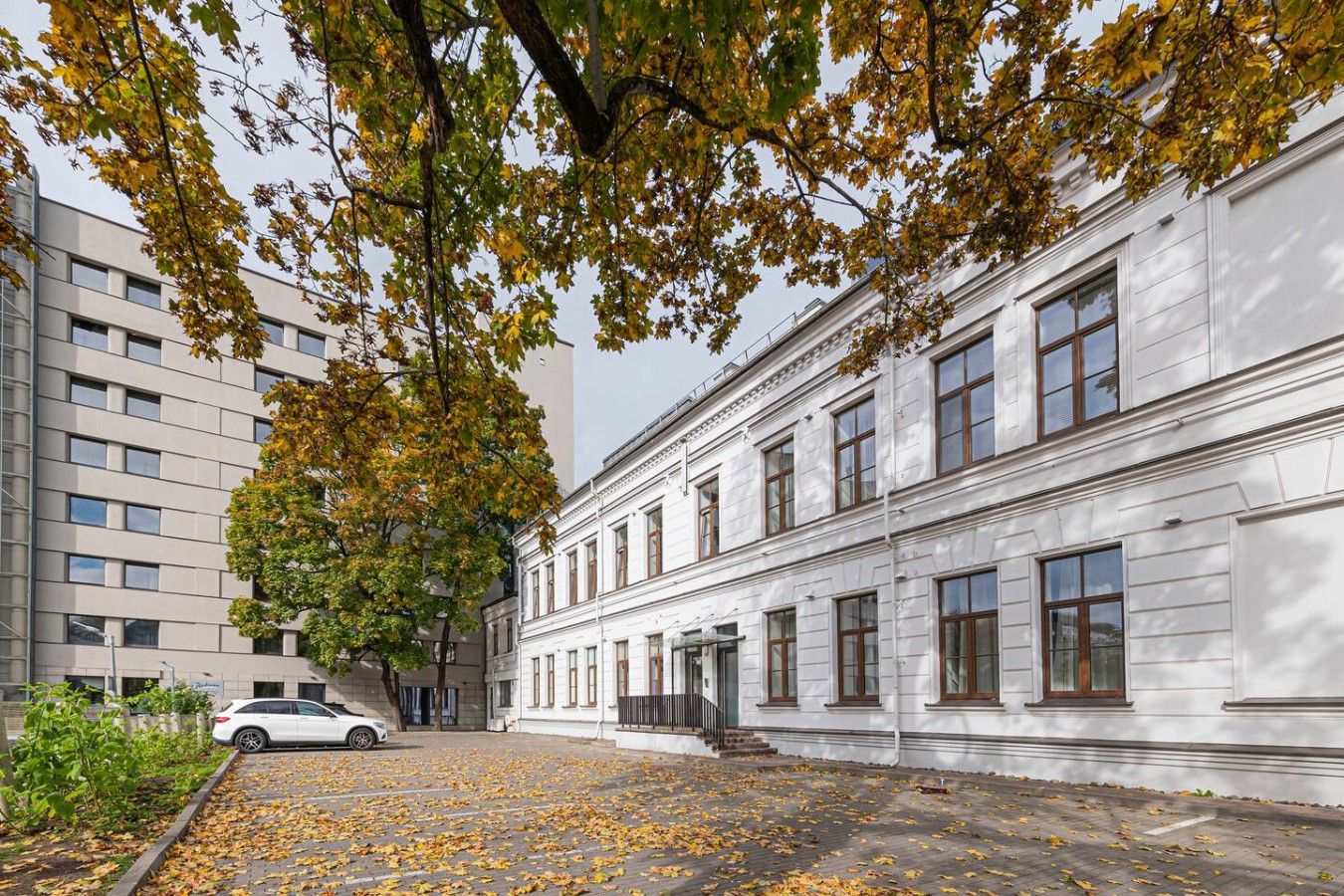 Un bâtiment à la façade classique, une cour pavée et une voiture garée.