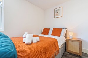 Ett hotellrum med en säng, kuddar, ett sängbord med en lampa och en inramad tavla på väggen.