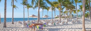 A beach with rows of sun loungers and umbrellas, palm trees, and a view of the ocean. - Luxury Junior Suite Cancun – Oceanfront Resort Getaway (Cancún)