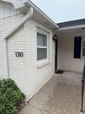 A residential building with a white brick exterior, a visible window, and a number '1310' on the wall. - Nebraska City Nook - Oak (1310 1st Ave) (Nebraska City)