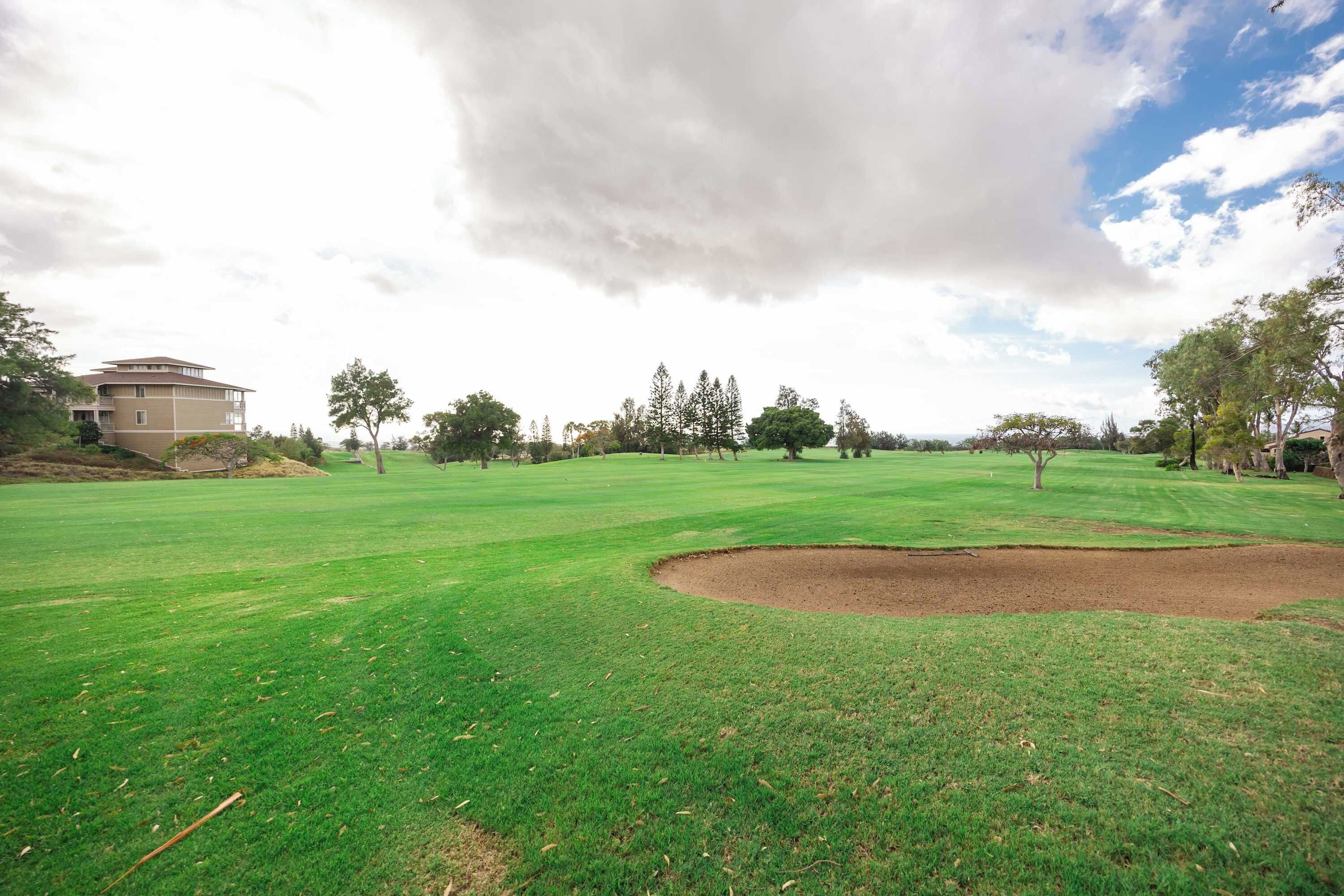 A golf course with a bunker, trees, and a building in the background.