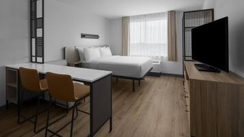 A hotel room with a bed, a desk with two chairs, a television, and a window with curtains.
