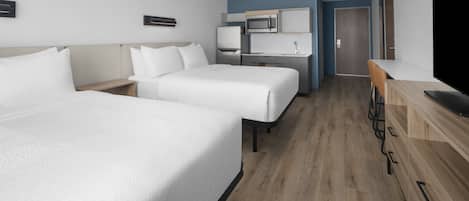 Habitación de hotel con dos camas, kitchenette, televisor y piso de madera.