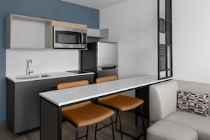 Una cocina moderna con microondas integrado, refrigerador y pileta. Hay dos taburetes de bar y una mesa de comedor.