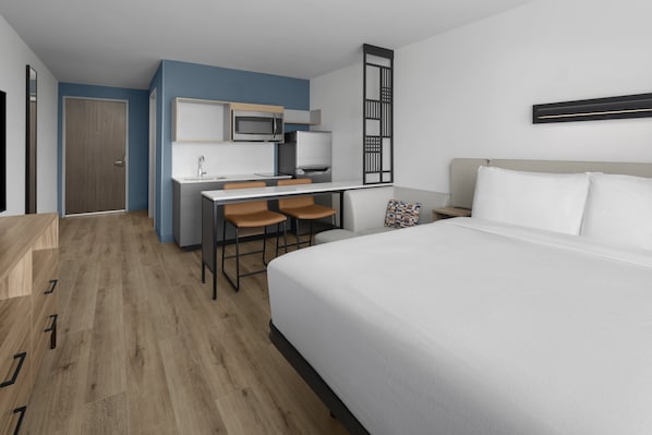 Una habitación de hotel con cama, escritorio con silla, microondas y refrigerador.