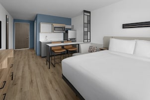 Una habitación de hotel con cama, escritorio con silla, microondas y refrigerador.