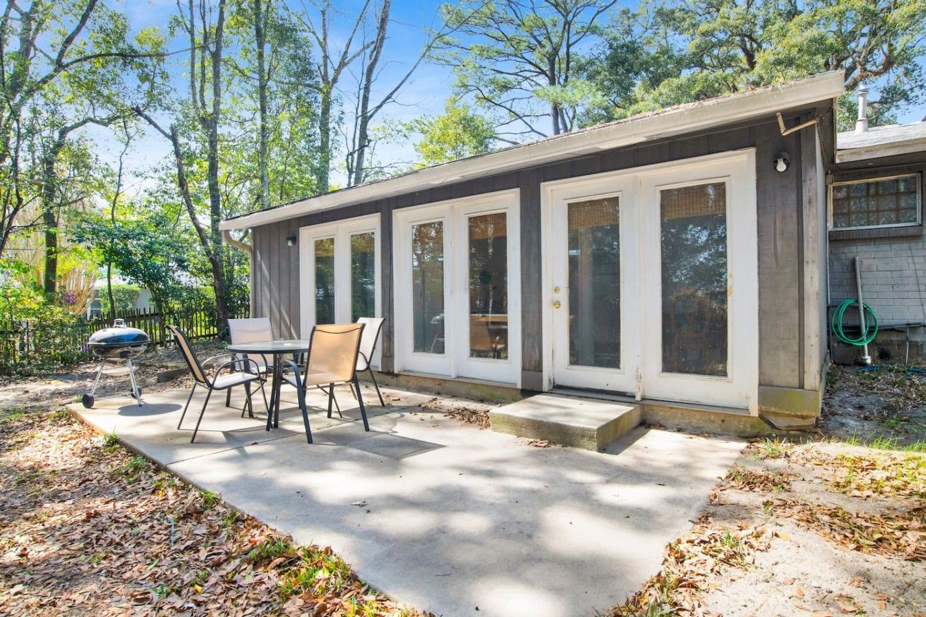A house with a covered patio, a barbecue grill, and a dining table with chairs.