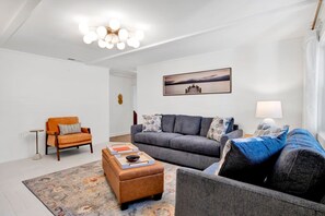 Ein Wohnzimmer mit einer Couch, einem Sessel, einem Hocker und einem Gemälde an der Wand.