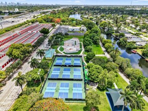 Ein Tennisplatz-Komplex mit mehreren Plätzen, umgeben von Grünflächen und einem Gewässer.