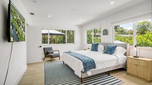 Ein modernes Schlafzimmer mit einem großen Bett, einem Sessel, einem Nachttisch und einem an der Wand befestigten Fernseher.