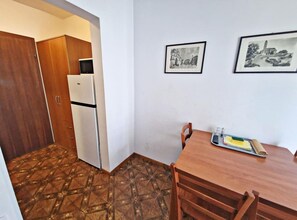 A small kitchenette with a refrigerator and a microwave, a wooden dining table with chairs, and two framed pictures on the wall. - Classic One Bedroom Apartment with Terrace and Sea View (Pag)
