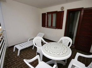 A balcony with a round table and four chairs, a small step, and a window with shutters. - Classic One Bedroom Apartment with Terrace and Sea View (Pag)