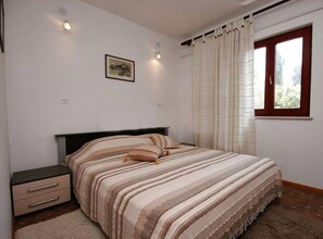 A bedroom with a bed, a nightstand, a window with curtains, and a wall-mounted light. - One Bedroom Apartment with Terrace (Pag)