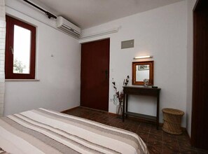 Un dormitorio con cama, una puerta de madera, un espejo y una mesita con lámpara.
