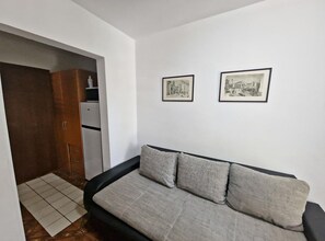 Una habitación pequeña y moderna con un sofá, dos cuadros en la pared y una zona de kitchenette.