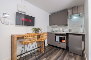 Eine kompakte Küche mit Einbauofen, Geschirrspüler und an der Wand befestigtem Fernseher, der 'NETFLIX' zeigt.