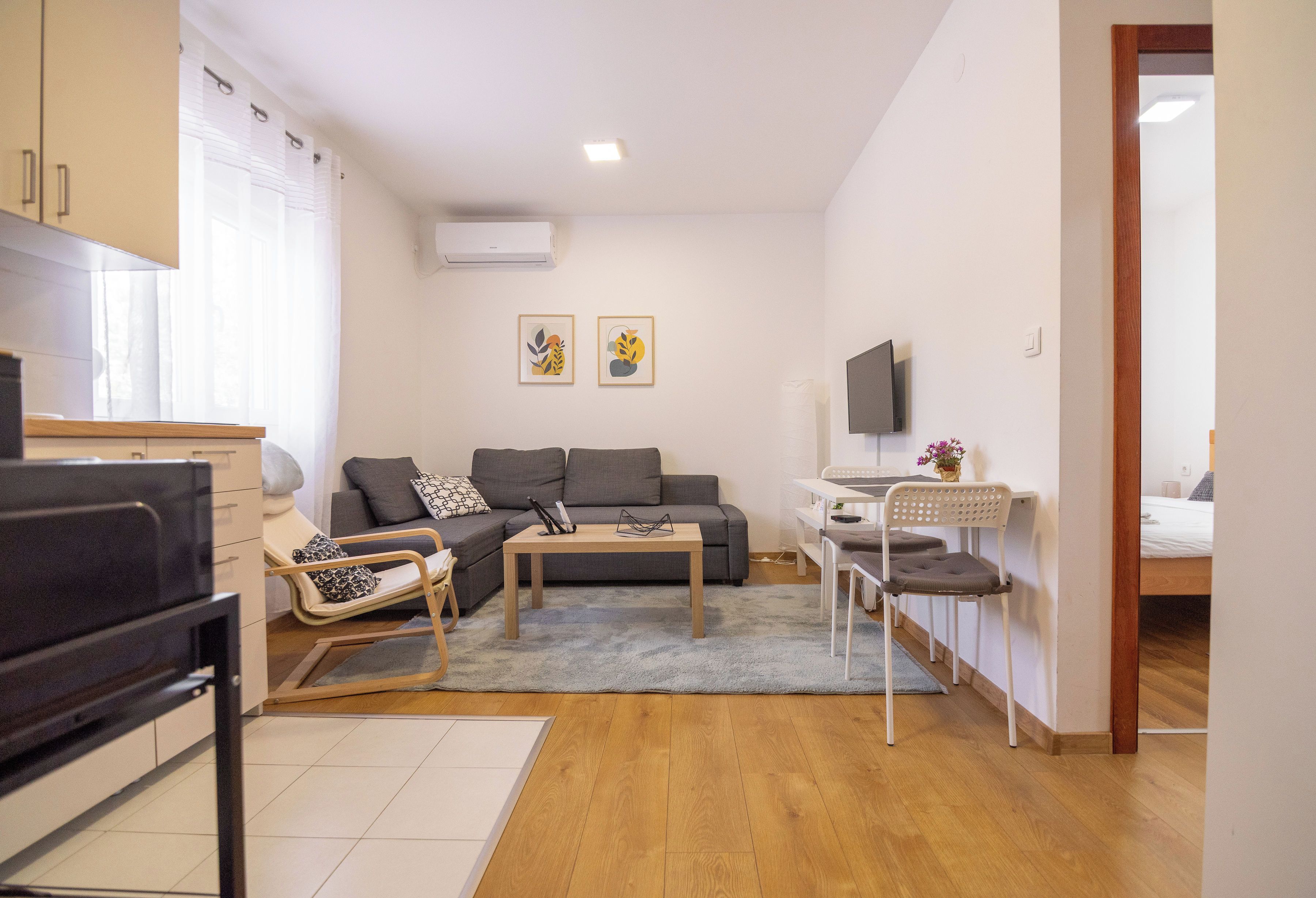 A modern living room with a sofa, a coffee table, a TV, and a dining area with chairs.