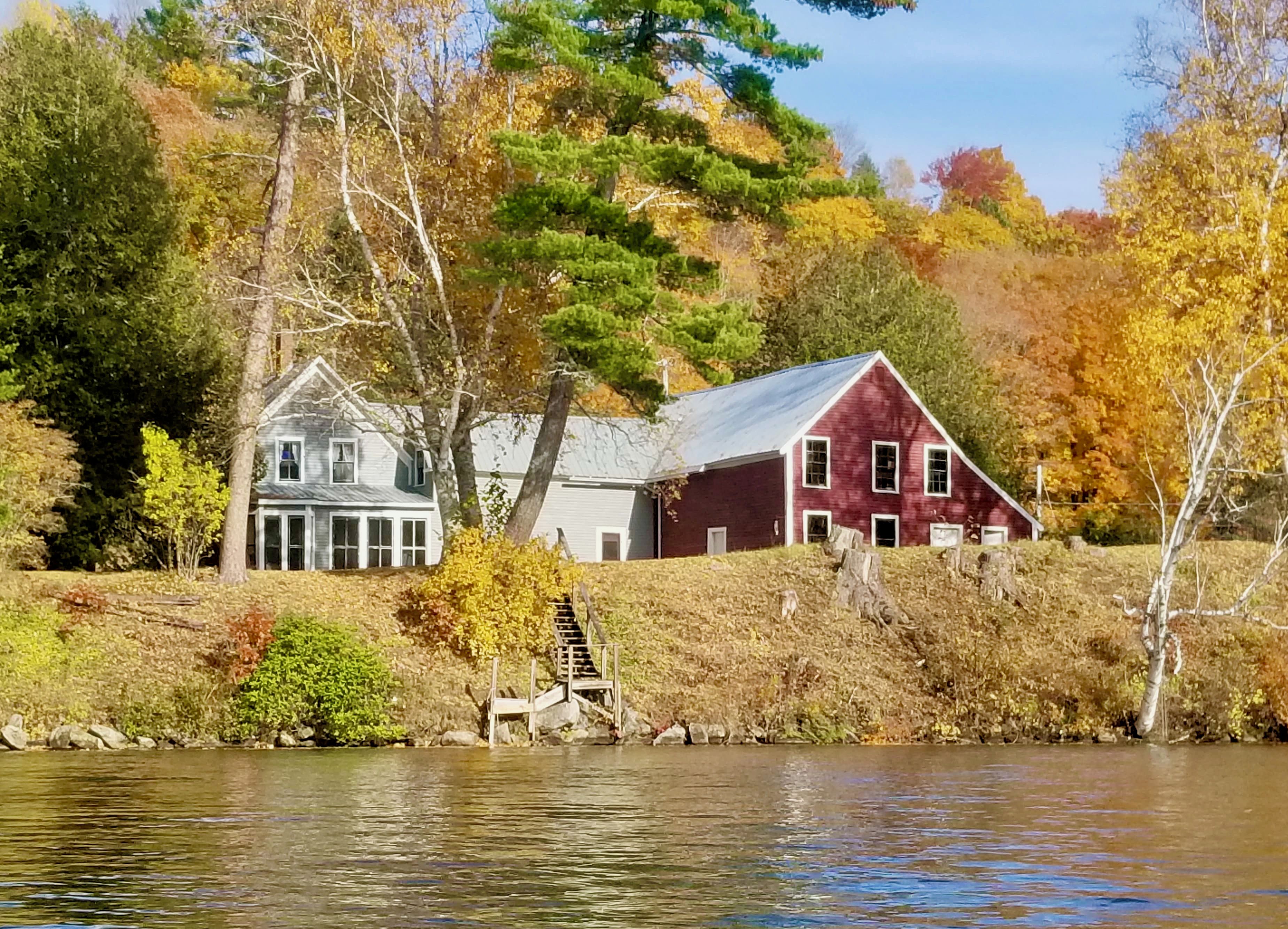 A lakeside view with two houses, one white and one red, surrounded by autumn foliage.