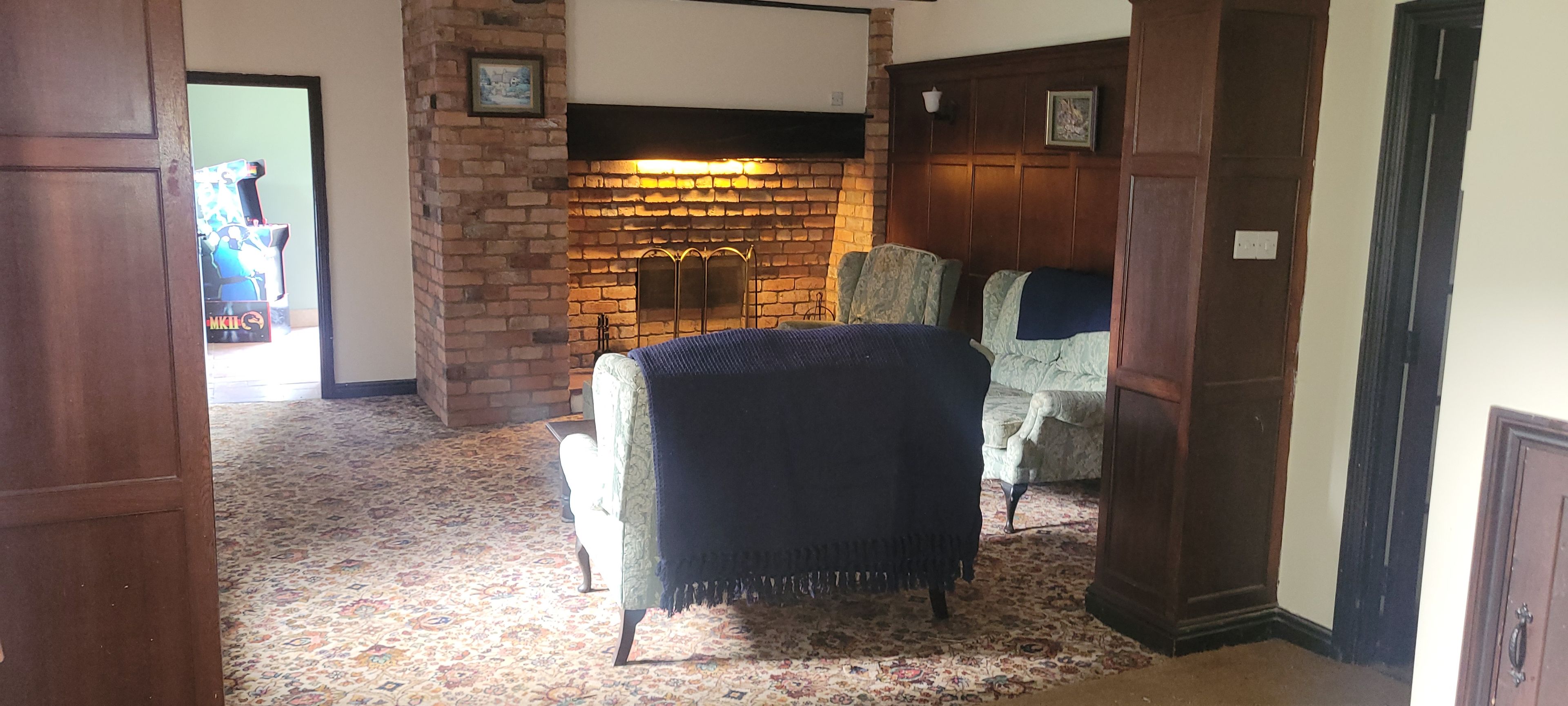 A room with a brick fireplace, a patterned carpet, and a chair with a throw blanket.