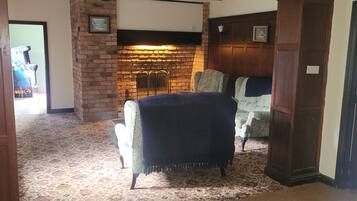 A room with a brick fireplace, a patterned carpet, and a chair with a throw blanket.
