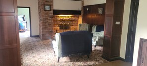 Ein Zimmer mit Kamin aus Backstein, einem gemusterten Teppich und einem Sessel mit Decke.