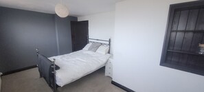 Ein Einzelbett in einem Zimmer mit dunkler Wand, weißer Decke und einem Fenster mit dunklem Rahmen.