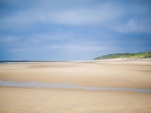 A wide sandy beach with gentle waves, a clear sky, and a distant green hill. - Cozy, very well-equipped vacation home for up to 5 people, within walking distance of the beach (Julianadorp)