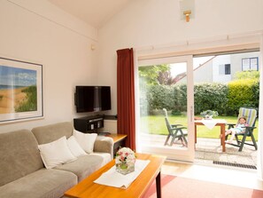 Ein Wohnzimmer mit einer Couch, einem Couchtisch, einem Fernseher und einer Glastür zum Außenbereich.