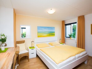 A bedroom with a bed, bedside tables, a chair, a window with curtains, and a painting on the wall. - Cozy, very well-equipped vacation home for up to 5 people, within walking distance of the beach (Julianadorp)