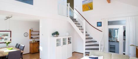 A spacious living area with a staircase, dining table, and seating.