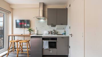 Een compacte kitchenette met een inbouwoven, een kleine koelkast, een magnetron en een spoelbak. Een flatscreen televisie is aan de muur bevestigd, waarop het Netflix logo te zien is.