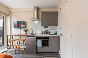A compact kitchenette with a built-in oven, a small refrigerator, a microwave, and a sink. There is a flat-screen TV mounted on the wall displaying the Netflix logo. - Sutherland Apartments - Apt 19 (London)