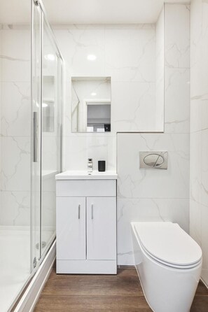 A modern bathroom with a glass shower enclosure, a white vanity with a mirror, and a toilet. - Sutherland Apartments - Apt 19 (London)