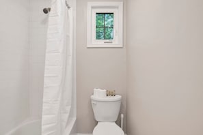 A bathroom with a white bathtub, a white toilet, and a window above the toilet. - College Cottage (Mobile)