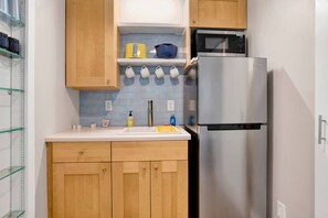 A modern kitchen with wooden cabinets, a stainless steel refrigerator, a microwave, and a sink. - College Cottage (Mobile)