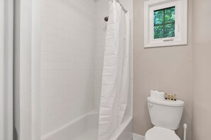 A bathroom with a white shower, a toilet, and a window with a view of trees. - College Cottage (Mobile)