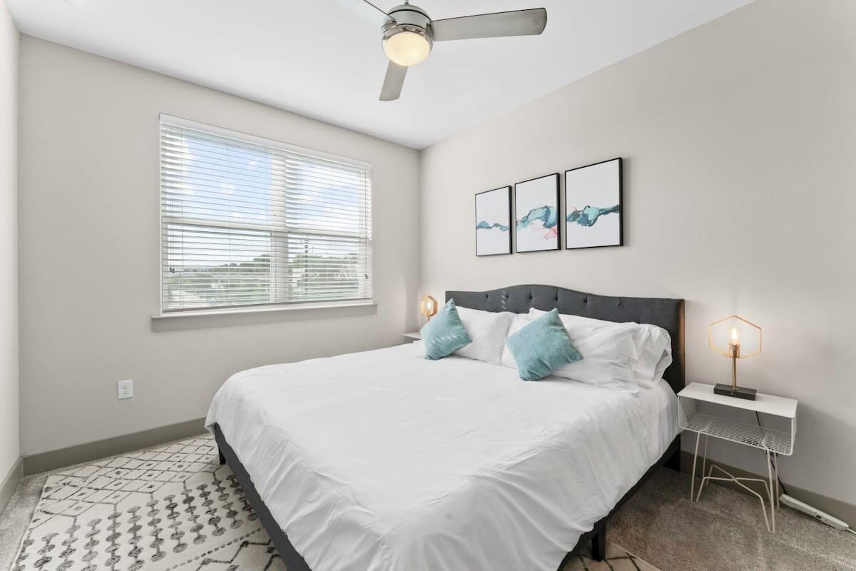 A bedroom with a bed, a ceiling fan, a window with blinds, and wall art.