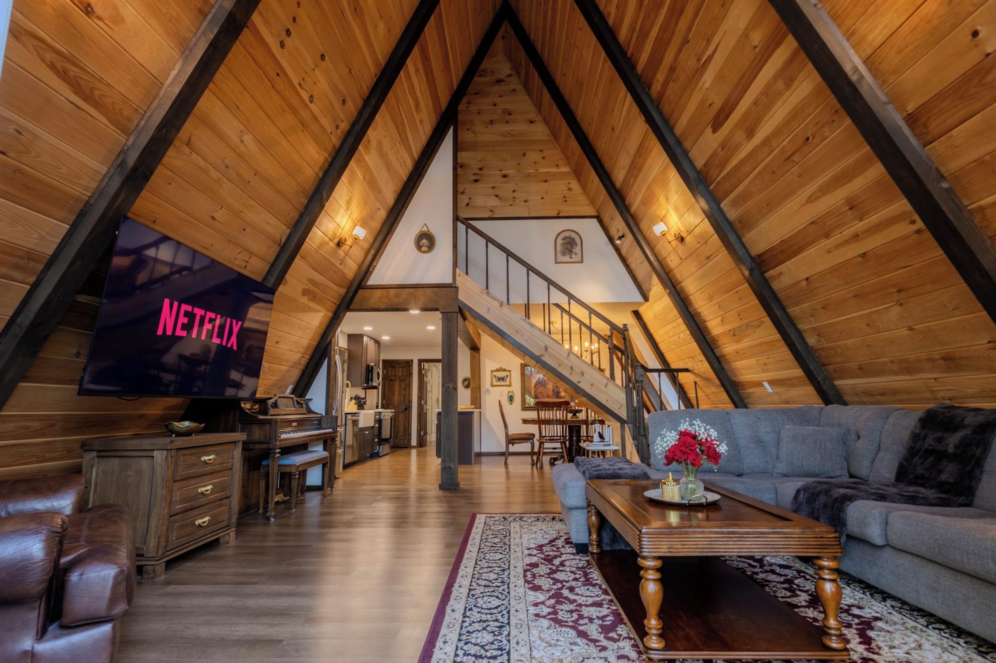 Ein Dachzimmer mit geneigtem Holzboden, einem Flachbildfernseher, einem Klavier, einer Couch und einer Treppe, die in eine weitere Ebene führt.