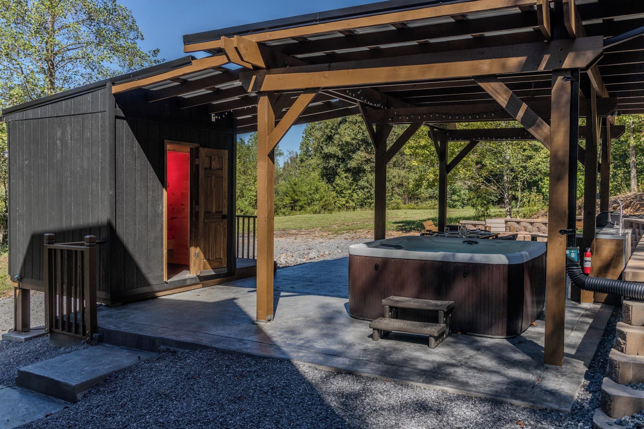 Ein überdachter Außenbereich mit Whirlpool, einer Holzterrasse und einem kleinen Gebäude mit roter Tür.