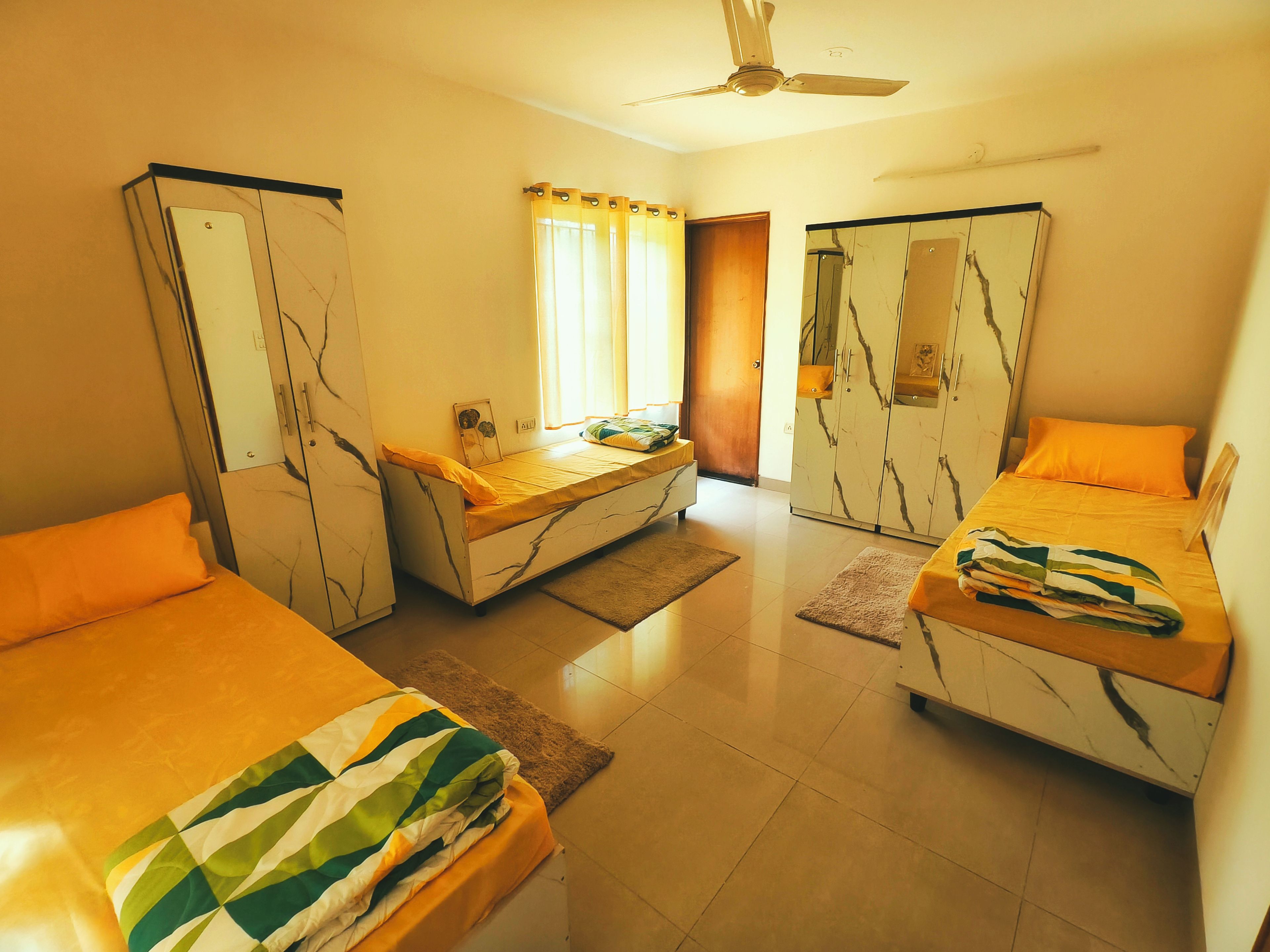 A hotel room with two beds, a wardrobe, a small table, and a window with curtains.