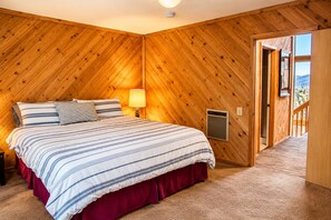 Ein Schlafzimmer mit Holzbalkendecke, einem Bett mit Streifenmuster-Bettwäsche, einem Nachttisch, einer Lampe und einem Thermostat.