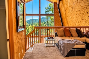 A cabin interior with a wooden deck, a sofa, and a view of a forested mountain. - Retro Alta Sierra A-Frame Cabin - Sequoia Forest (Wofford Heights)