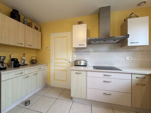 Une cuisine avec des meubles de couleur claire, une hotte de cuisinière en acier inoxydable et un grille-pain posé sur le plan de travail.
