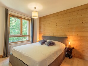 Ein Schlafzimmer mit einem hölzernen Kopfteil, einem Bett mit weißen Leinen, einer Nachttischlampe und einem Fenster mit Vorhängen.