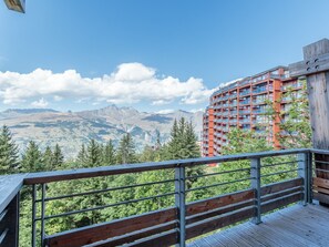 A balcony with a metal railing overlooking a mountainous landscape and a red building with balconies. - Spacious apartment, mountain view - 5 guests (Les Arcs 1800)