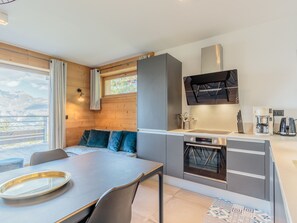 A modern kitchen with a built-in oven, a coffee maker, and a dining area with a table and chairs. - Spacious apartment, mountain view - 5 guests (Les Arcs 1800)